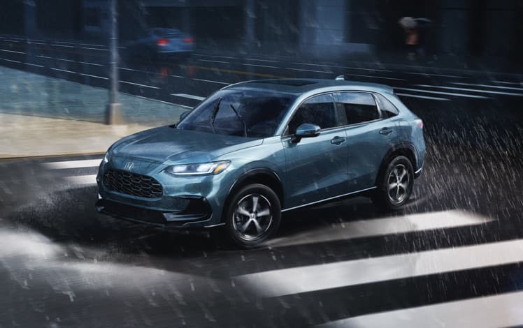 Front driver-side view of the 2025 Honda HR-V EX-L in Nordic Forest Pearl, driving in an urban environment during a rainstorm.